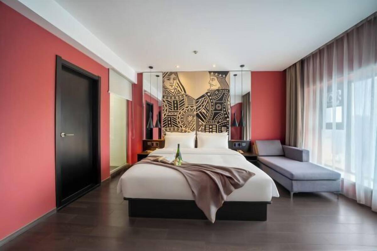 A modern hotel room with a large bed, a seating area, and a decorative wall piece.