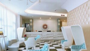 Un hall d'entrée moderne avec un sol à carreaux, des fauteuils blancs et bleu clair, un comptoir d'accueil en marbre et un lustre.