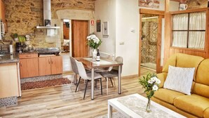 A cozy living area with a wooden ceiling, stone walls, a dining table with chairs, a sofa, and a kitchen with granite countertops and wooden cabinets.