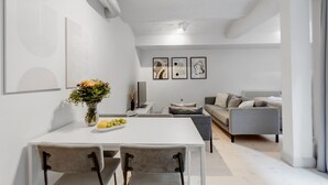 Un salon moderne avec un canapé gris, une table à manger et deux chaises, ainsi qu’un vase rempli de fleurs.