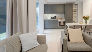Una sala de estar moderna con sofá y sillón, un comedor y una cocina al fondo.