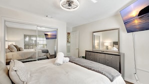 A modern bedroom with a large bed, a dresser, a television, and a sliding door closet.