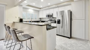 A modern kitchen with white cabinetry, stainless steel appliances, and a marble countertop island with bar stools.