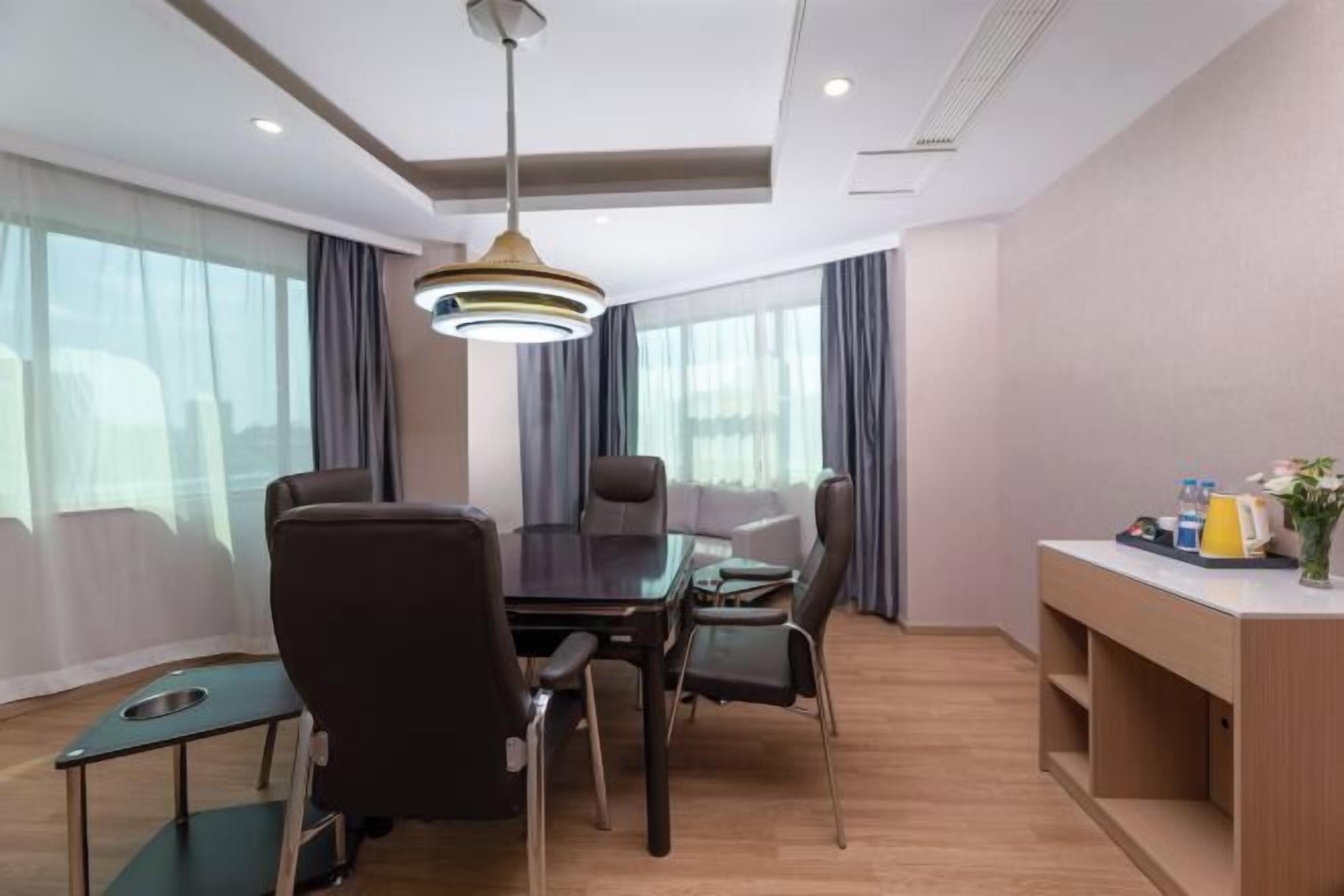 Una habitación de hotel moderna con comedor, sofá, una pequeña mesa y un gran ventanal con cortinas.