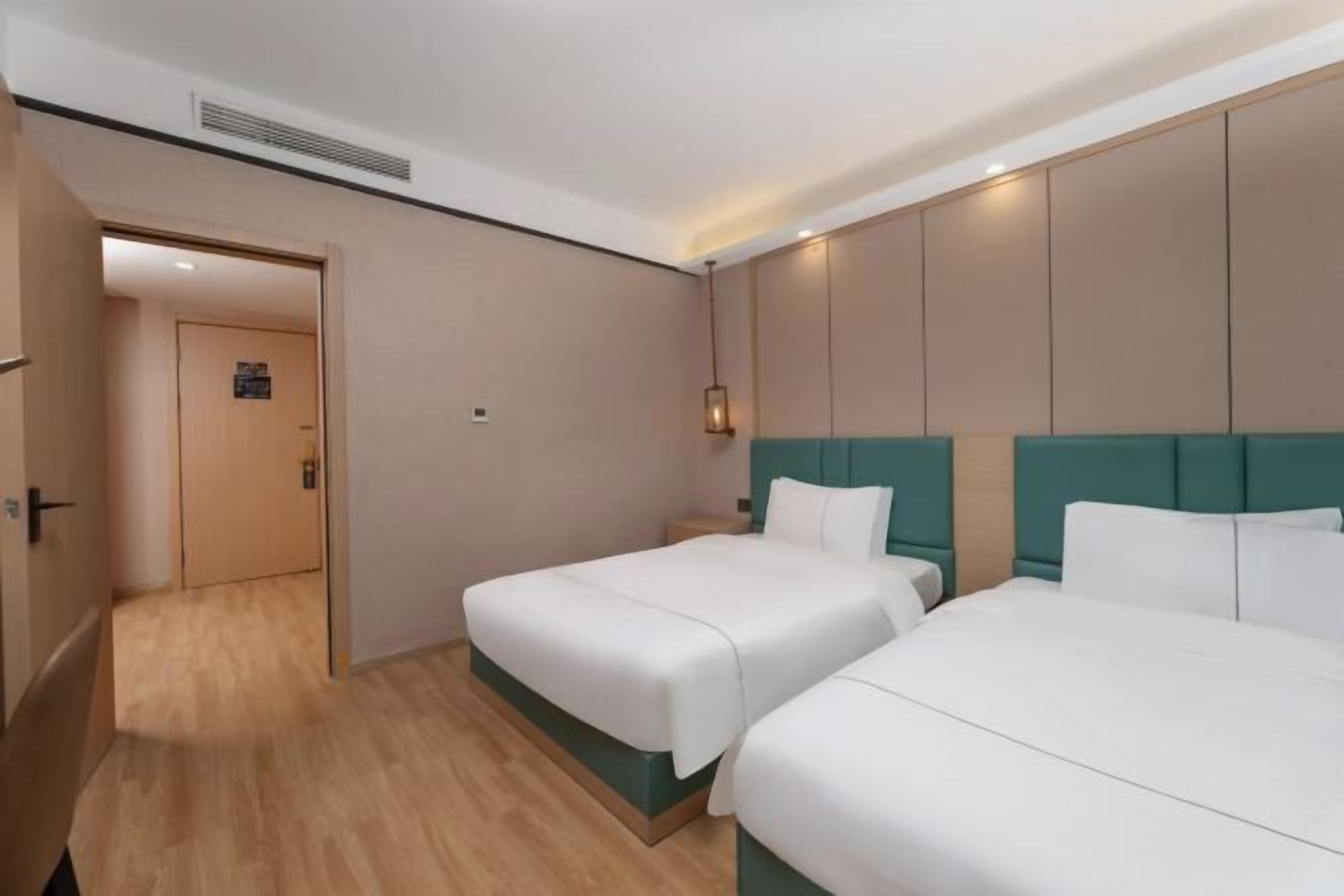 A hotel room with two beds, a wooden floor, and a teal headboard.
