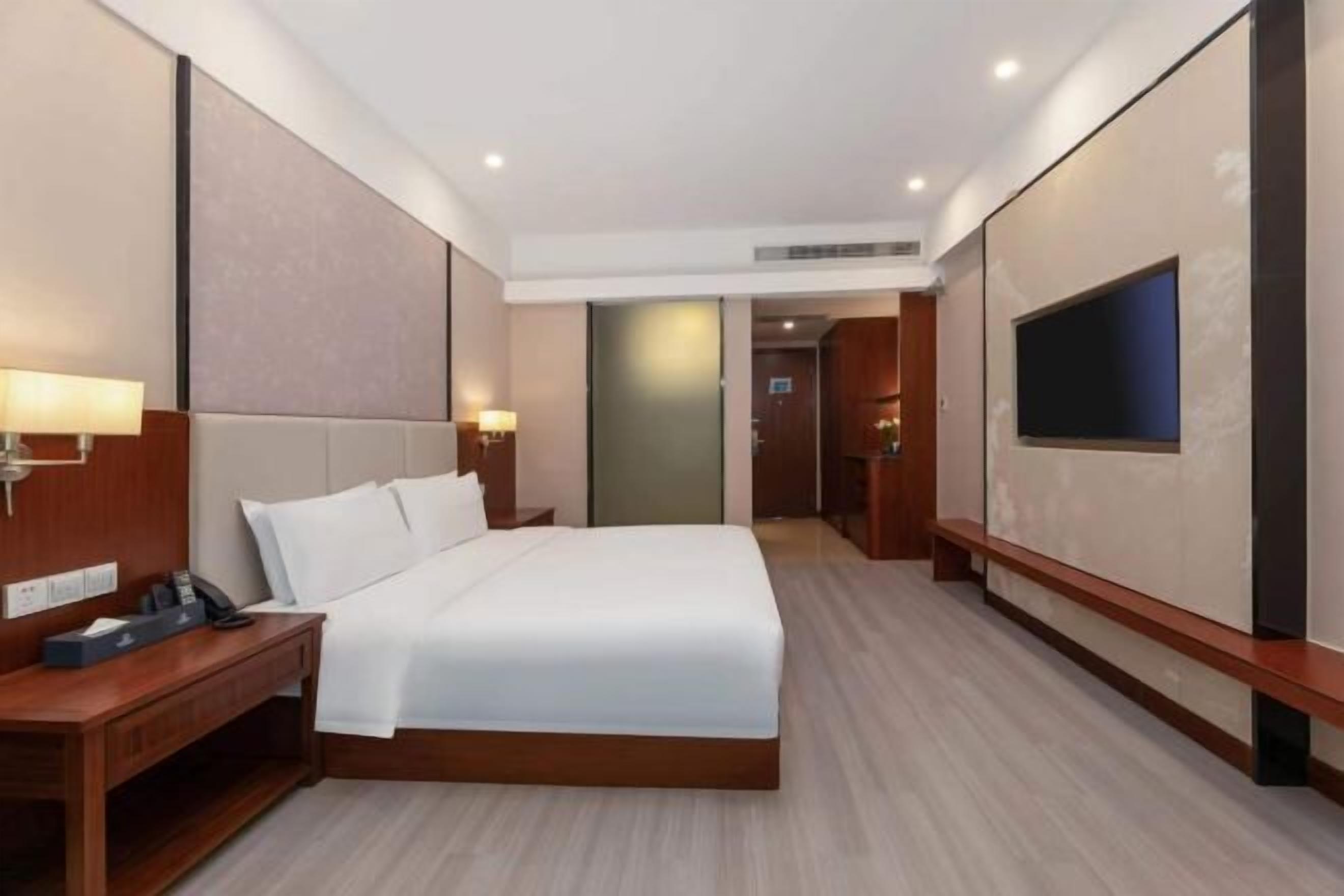 Camera d'albergo con un letto grande, comodini, una televisione e una porta che dà sul bagno.