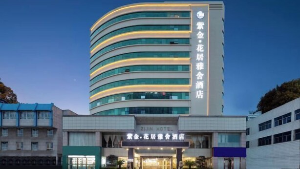 Un hotel con fachada moderna y curva, señalización que indica que es el ZIJIN HOTEL, y una entrada visible con un cartel en un idioma extranjero.