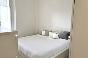 A bedroom with a bed, pillows, a nightstand, and a window.