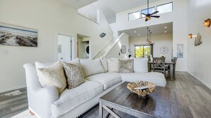 A spacious living room with a sectional sofa, a dining area with wooden chairs, a staircase, and a ceiling fan. - 2 Oceanfront Homes w/ Rooftop Deck, Views & Steps to the Sand (Oceano)