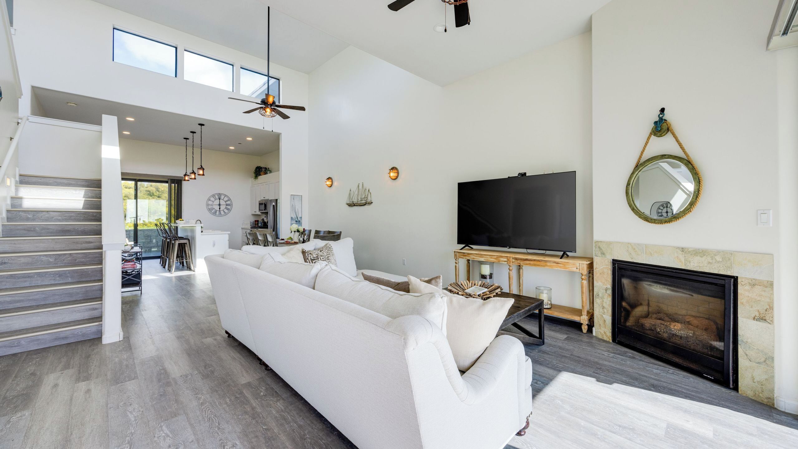 A spacious living area with a white sofa, a fireplace, a television, and a staircase leading to an upper level.