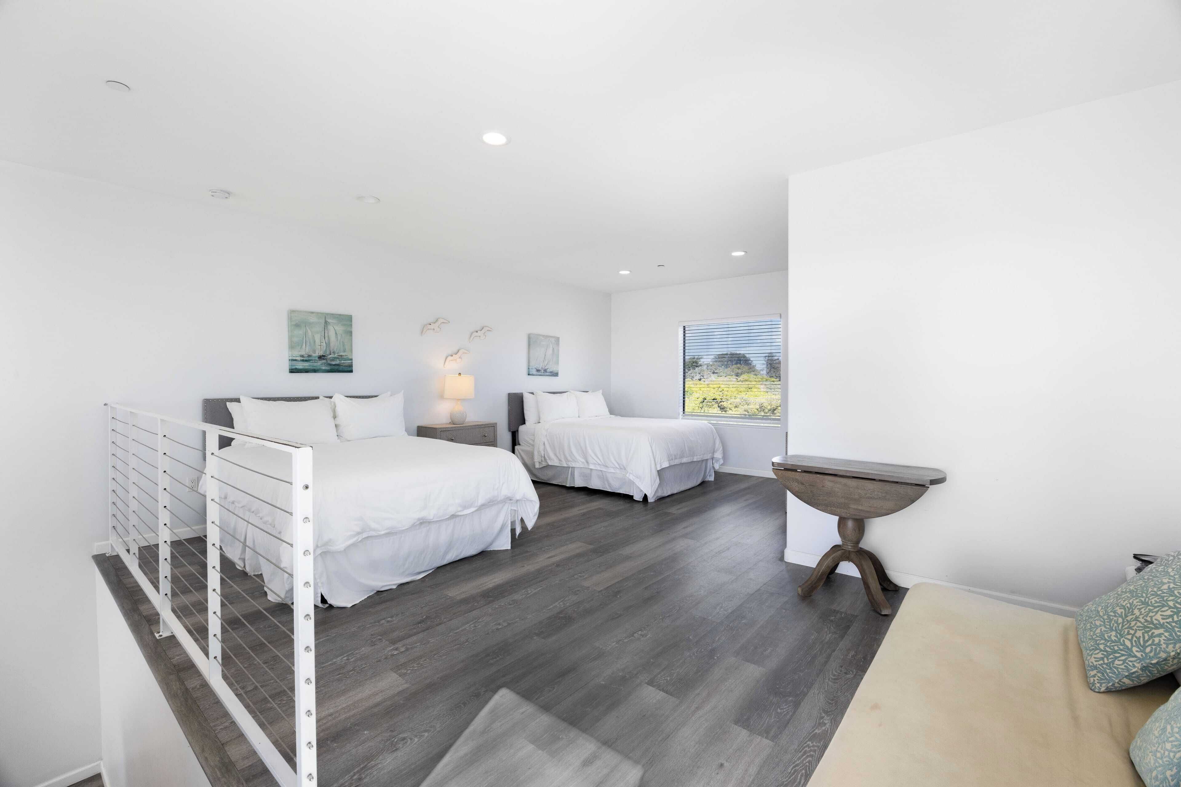 A bedroom with two beds, a small table, and a window with a view.