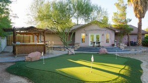 Il s’agit d’une propriété résidentielle dotée d’un jardin avec un green d’entraînement au golf, d’une pergola en bois et d’un escalier en pierre menant à la porte d’entrée.