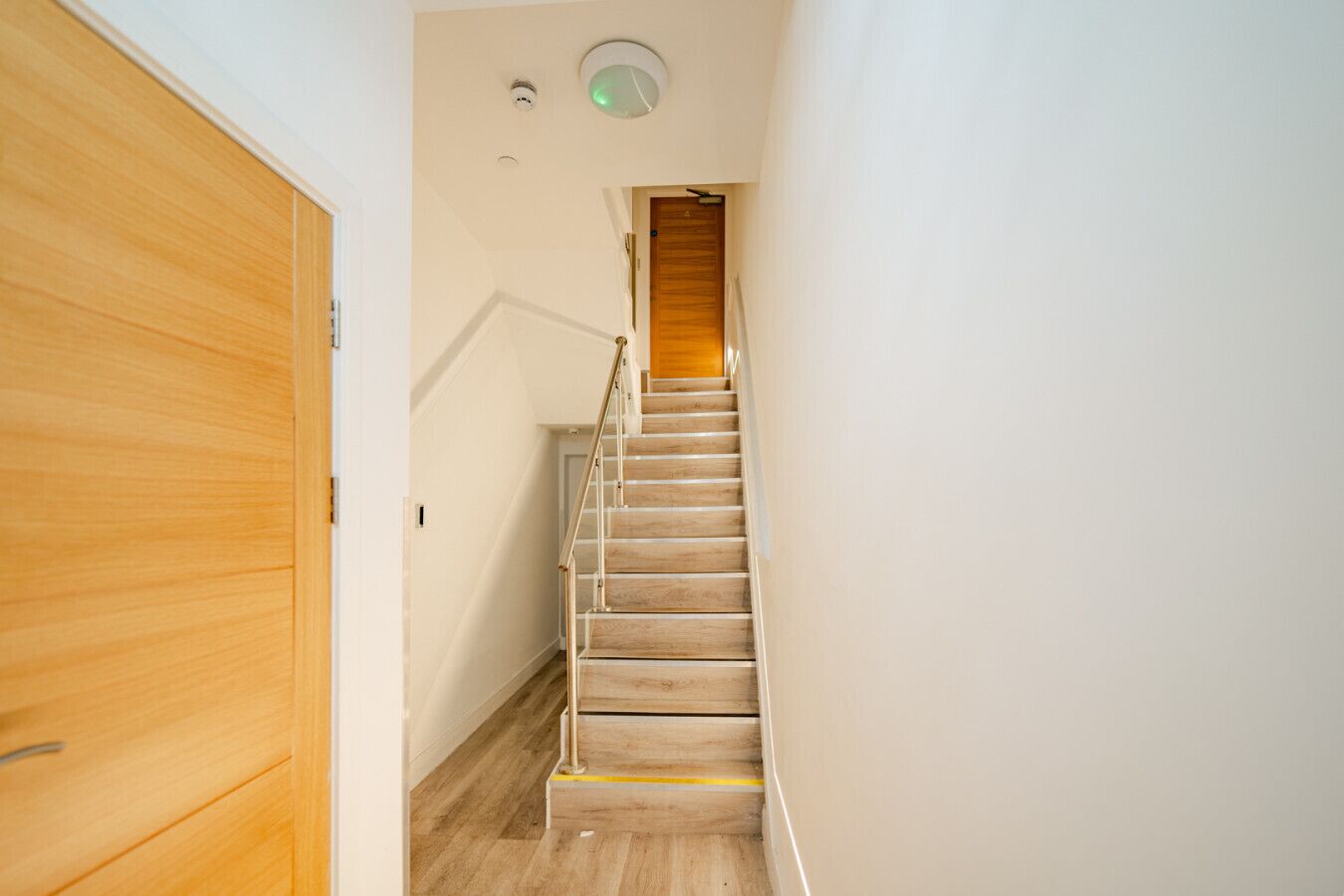 Eine Holztreppe mit Geländer, eine Holztür und eine Deckenleuchte.
