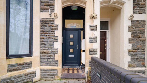 A building with a stone facade, a black door with a window, and a small porch area.