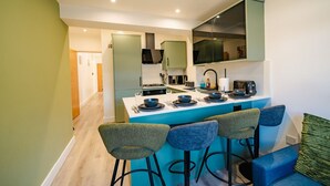A modern kitchen with a central island, bar stools, and a dining area.