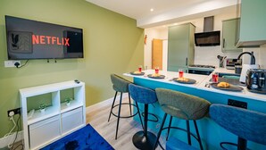 A modern kitchen with a bar area, a flat-screen TV, and a dining setup with chairs and a table.