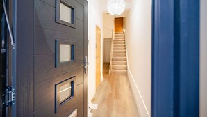 A hallway with a dark wooden door, a staircase, and a chandelier.