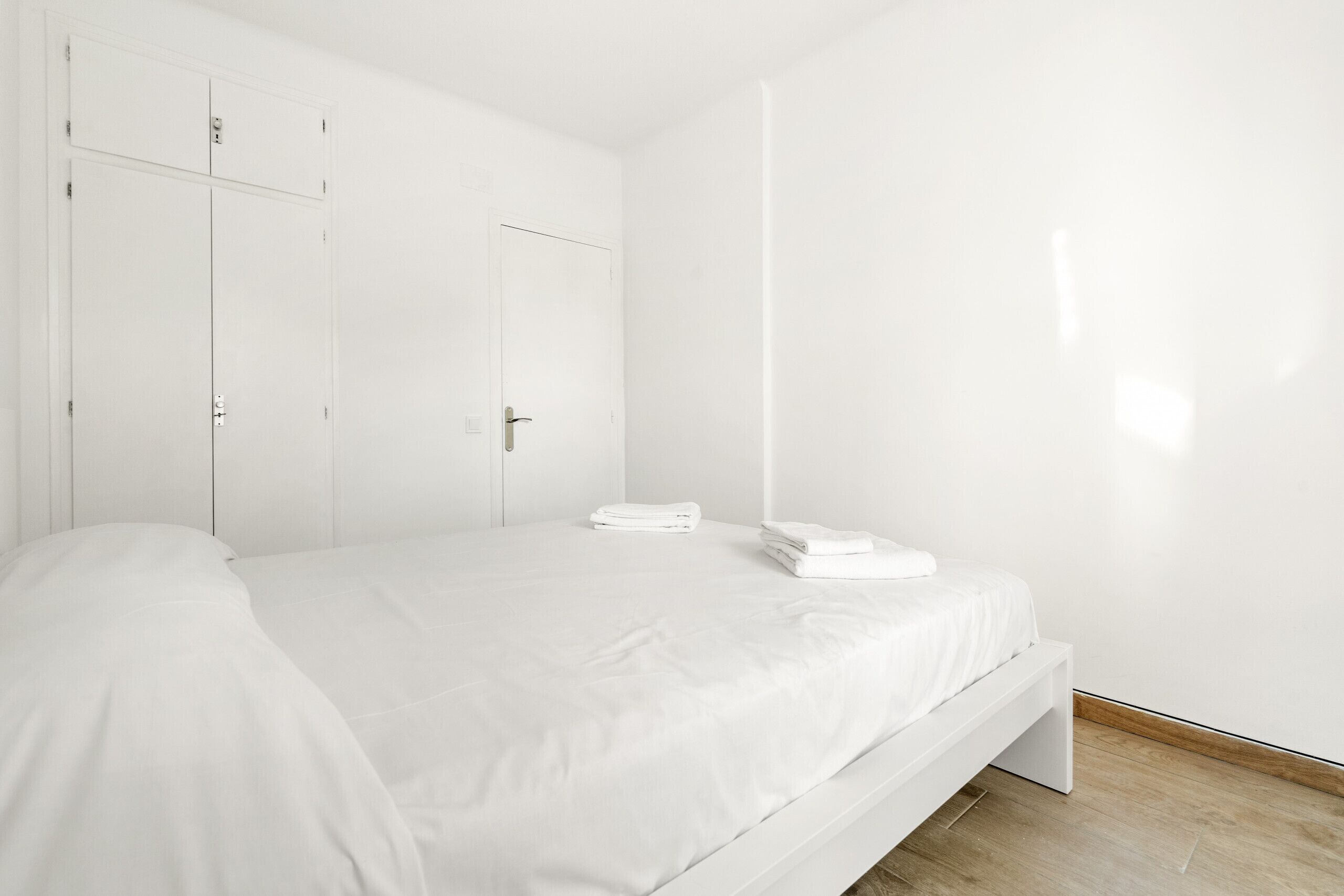 A minimalist bedroom with a single bed, a wardrobe, and a door.