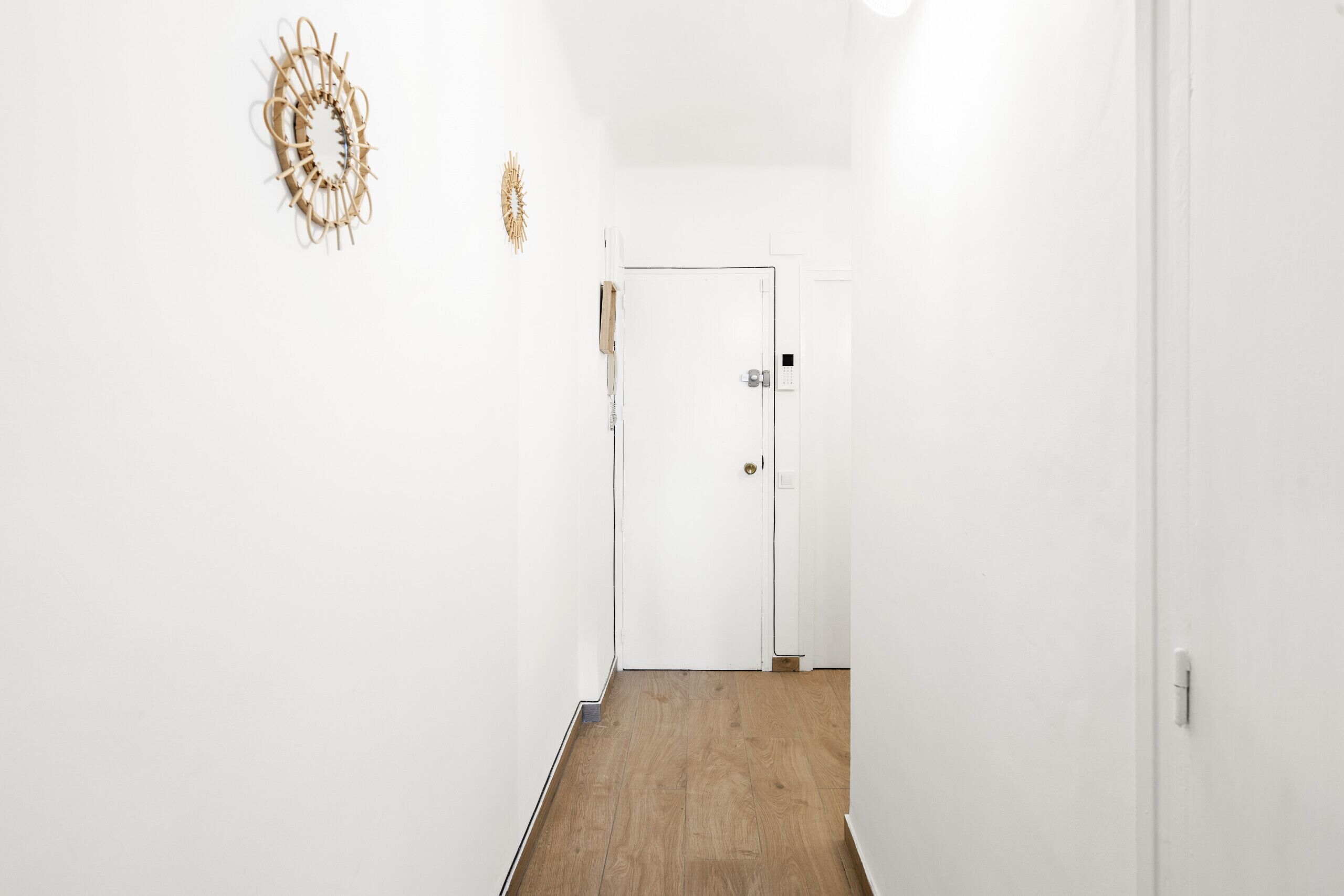 A narrow hallway with a wooden floor and white walls. There is a door at the end of the hallway.