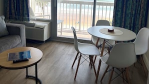 A room with a balcony overlooking the sea, furnished with a sofa, a round table, and chairs.