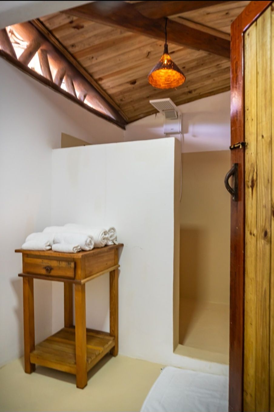 Una habitación con una mesa de madera, toallas, techo de madera y una puerta de madera.