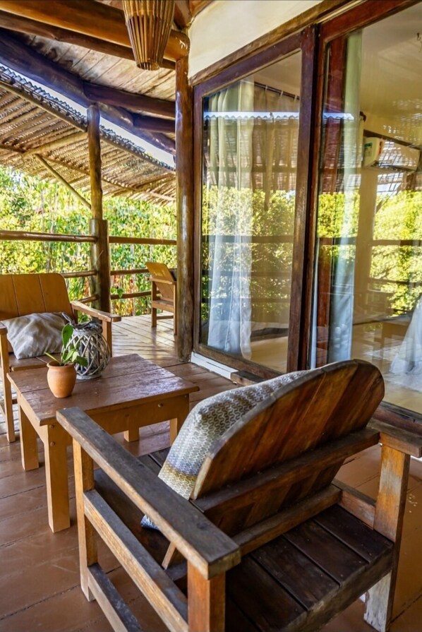 A wooden deck with a bench and table, large windows, and a view of greenery. - Terrazza Trancoso Hotel Boutique (Porto Seguro)