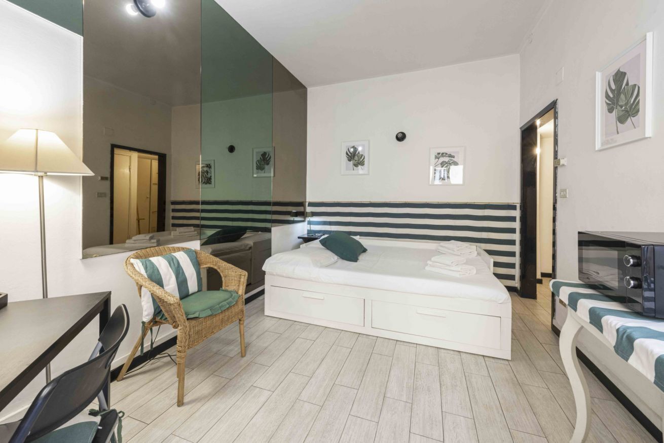 A hotel room with a bed, a chair, a table, and a microwave.