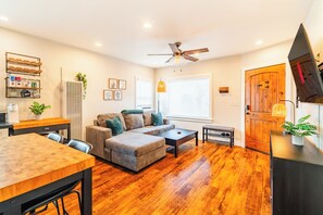 A modern living room with a wooden floor, a sofa, a coffee table, and a dining area with a wooden table and chairs. - Charming 2-Bedroom apartment / 10-min walk to the Beach / Parking Stall / AC (Long Beach)