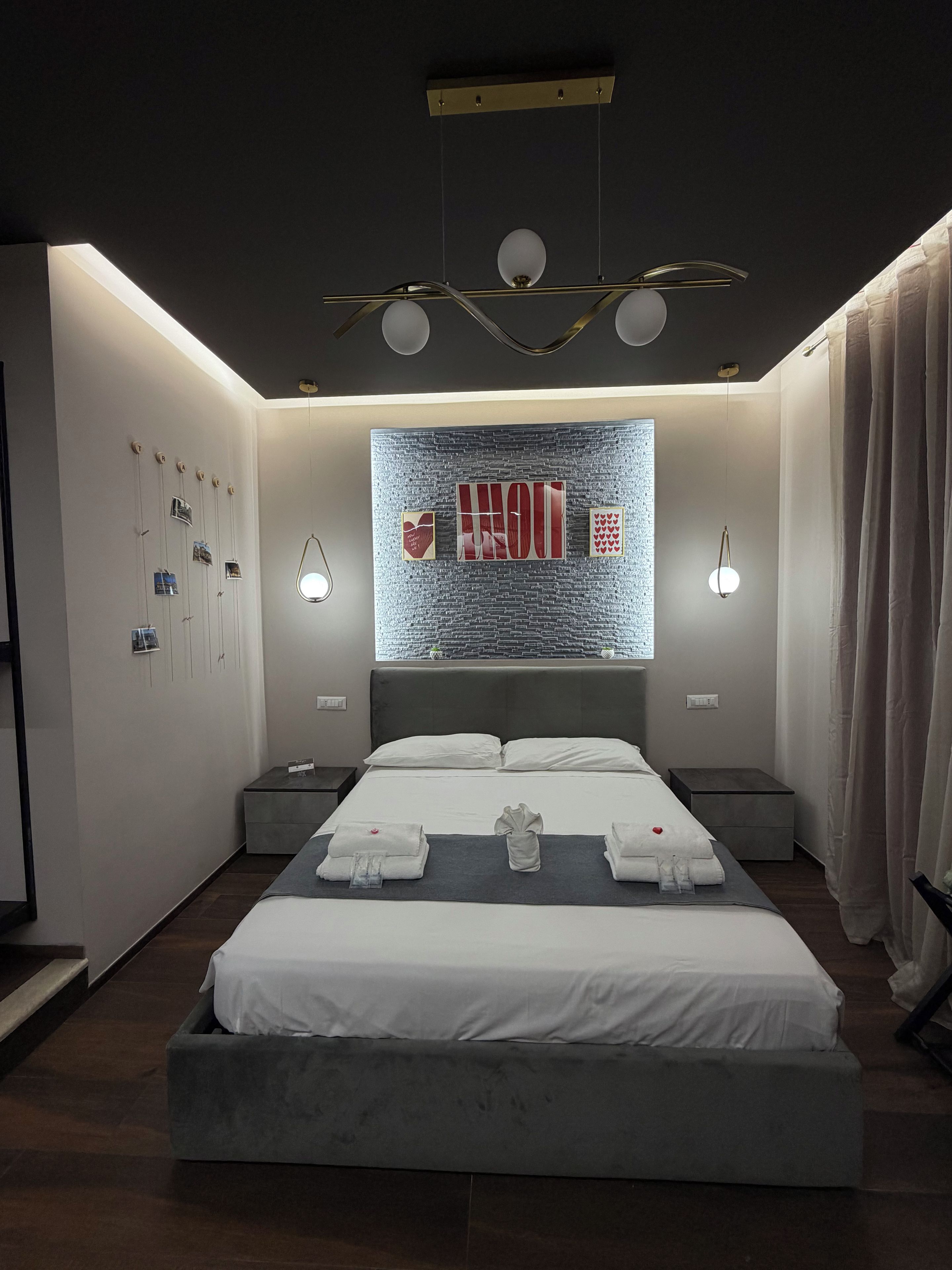 A modern hotel room with a large bed, bedside tables, a wall art piece, and a ceiling light fixture.