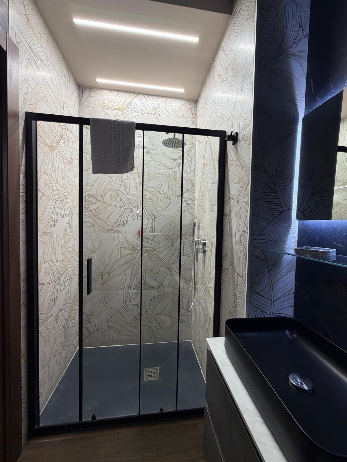 A modern bathroom with a glass-enclosed shower, a dark bathtub, and a marble countertop.