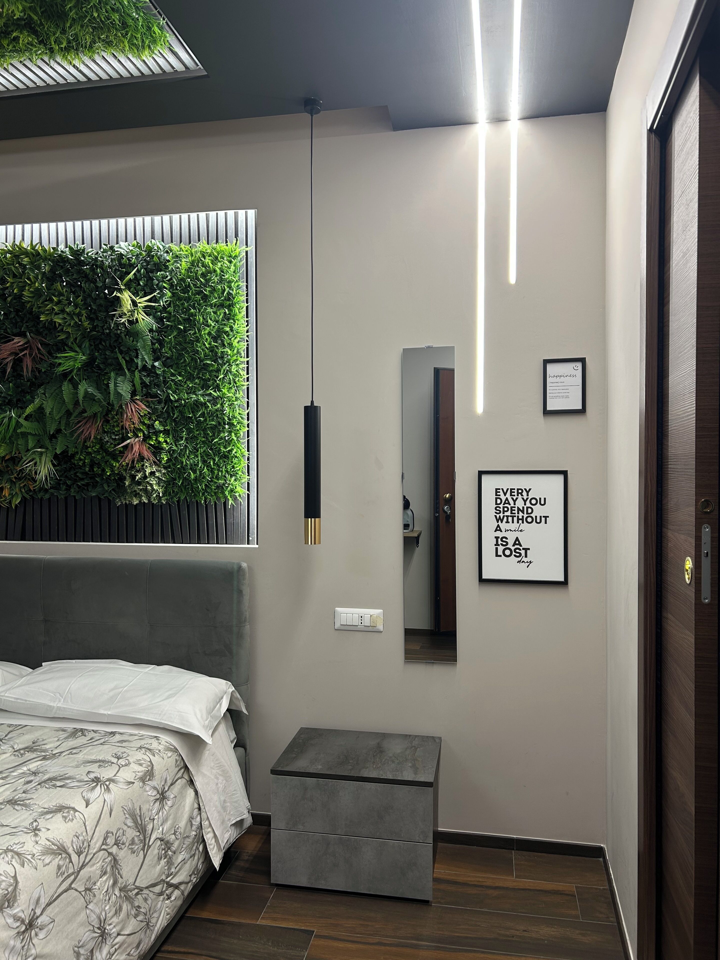 A modern bedroom with a bed, a grey bench, a green wall with plants, a mirror, and motivational wall art.