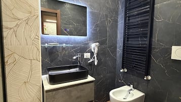 Uma casa de banho moderna com painel de parede de mármore, lavatório embutido, toucador, bidé e sanita.