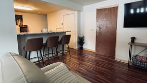 Una sala de estar con sofá, un área de cocina con barra y una puerta de madera.