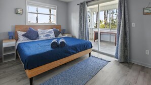 Ein Schlafzimmer mit einem großen Bett, einem Nachttisch, einem Fenster und Blick ins Freie.