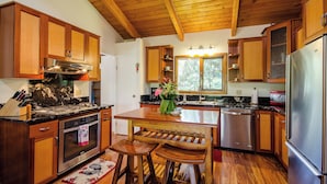 Una cucina con mobili in legno, un frigorifero in acciaio inossidabile e un tavolo da pranzo in legno con due sgabelli.