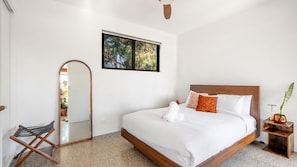 A bedroom with a bed, a mirror, a window with a view, and a small table with a plant.