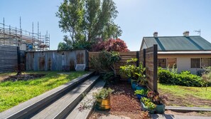Ein Garten mit einer Holzterrasse, einem Metallzaun und verschiedenen Kübelpflanzen.