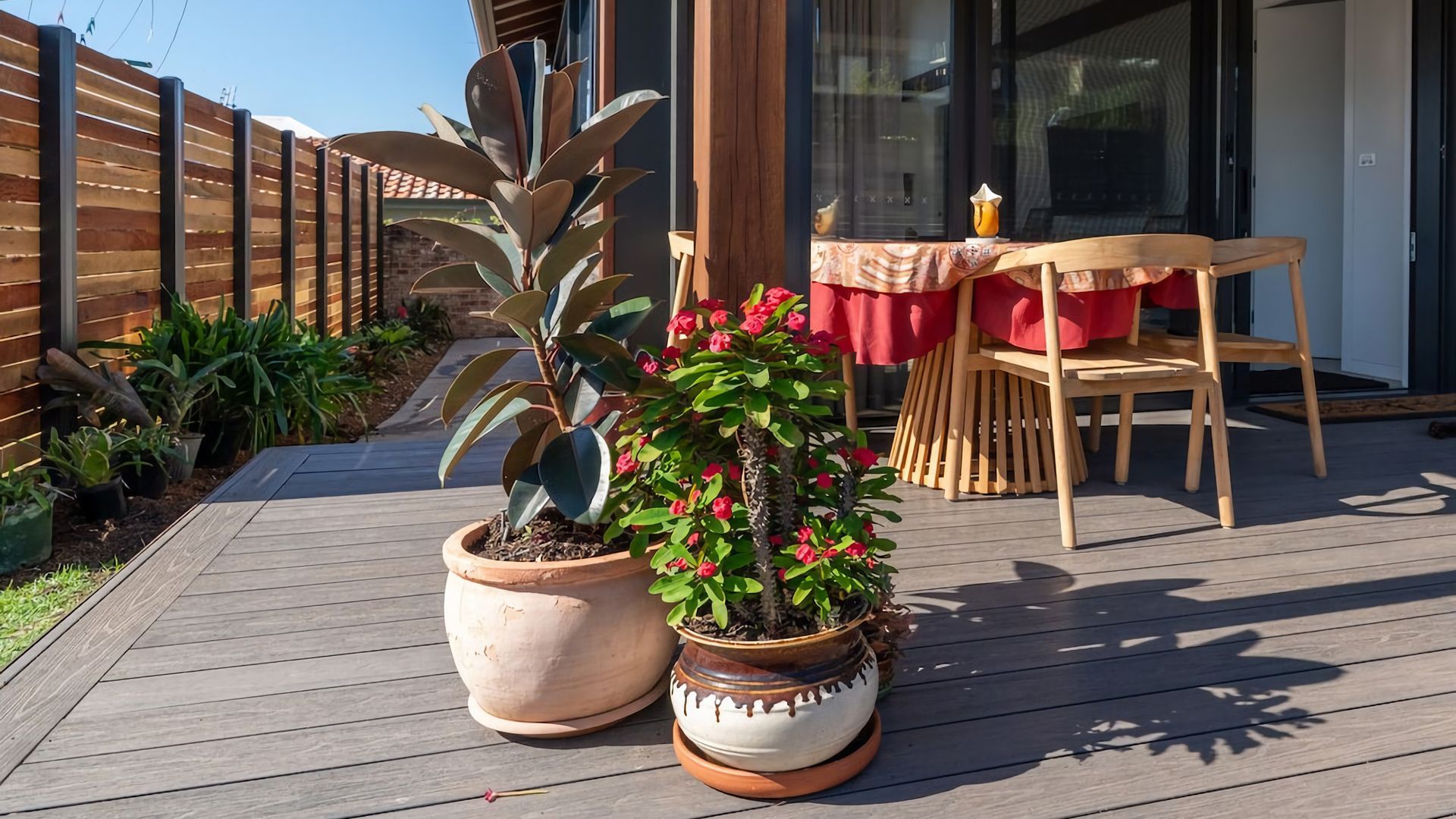A wooden deck with potted plants and a table with chairs.