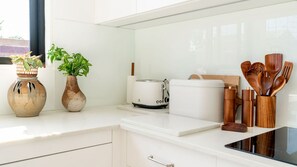A modern kitchen with white cabinetry, a toaster, a white kettle, wooden utensils, and two potted plants.