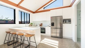 Eine moderne Küche mit einer zentralen Kochinsel, Barhocker, einem Edelstahlkühlschrank und einem großen Fenster, das für natürliches Licht sorgt.