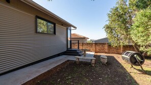 Una casa moderna con un porche cubierto, una mesa de piedra y un barril.