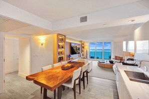 A modern kitchen with a wooden dining table, white chairs, and a built-in island with a sink.