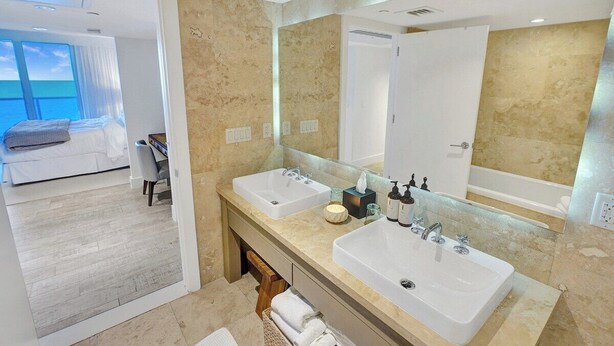 Um banheiro moderno com duas pias, um espelho grande e vista para um quarto com varanda.