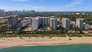 Paisagem costeira com edifícios altos, uma praia e o horizonte de uma cidade ao longe.