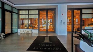 Entrada de hotel com uma grande porta de vidro, um balcão de recepção e uma placa com o nome do hotel.