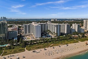 A coastal cityscape with high-rise buildings, a beach with numerous sun loungers, and a clear sky.