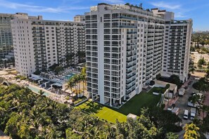 A high-rise hotel with multiple balconies, a swimming pool, and a well-maintained lawn.