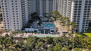 Um hotel moderno com vários sacadões, piscina no terraço e muita vegetação.