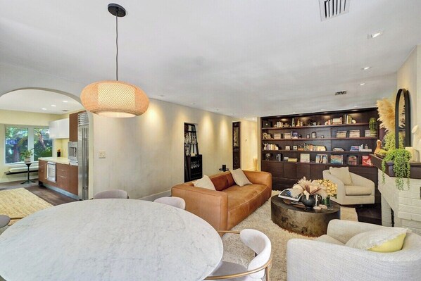 A modern living room with a round marble table, leather sofa, and a bookshelf filled with books.