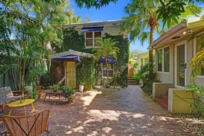 A courtyard with a paved walkway, outdoor furniture, and lush greenery.